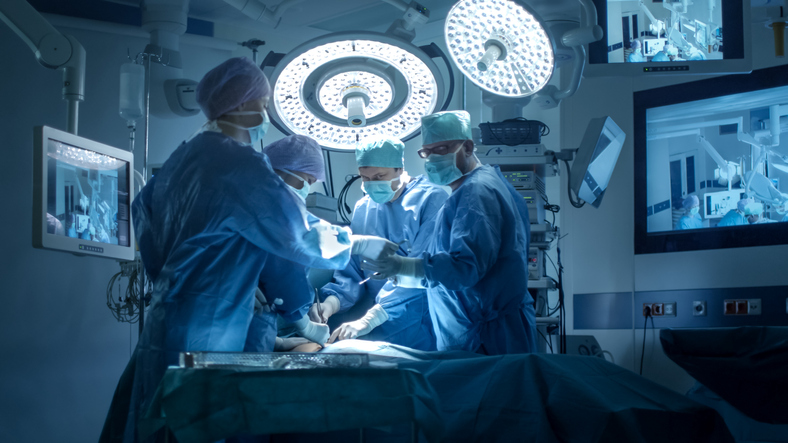 A crew of surgeons and their equipment performing herniated disk surgery on a patient in a surgery center.