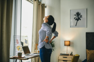 Rearview shot of a young woman suffering with back pain while working from home