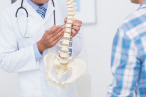 male spinal doctor pointing to model of spine in front of patient