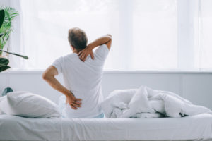 back view of man sitting on bed and suffering from back pain