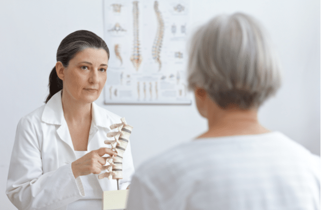 doctor of orthopedics showing her senior patient a slipped disk on a backbone model.