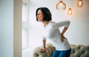 Adult woman is holding her lower back, suffering from unbearable pain.