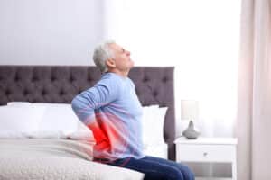 Fit woman experiences pain in her upper arm due to a herniated disc. Older man winces on his bed from lower back pain.