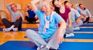 Fit woman experiences pain in her upper arm due to a herniated disc. Mature woman in fitness class freely moves her neck while sitting on a mat.